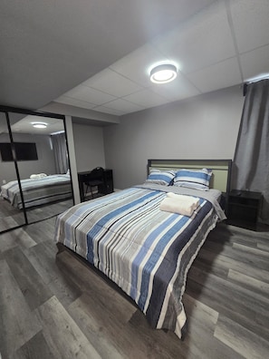 A bedroom with a bed, a mirror, a bedside table, a TV, and a ceiling light. - Yekky Room 101-Place in Devonshire Park (Winnipeg)