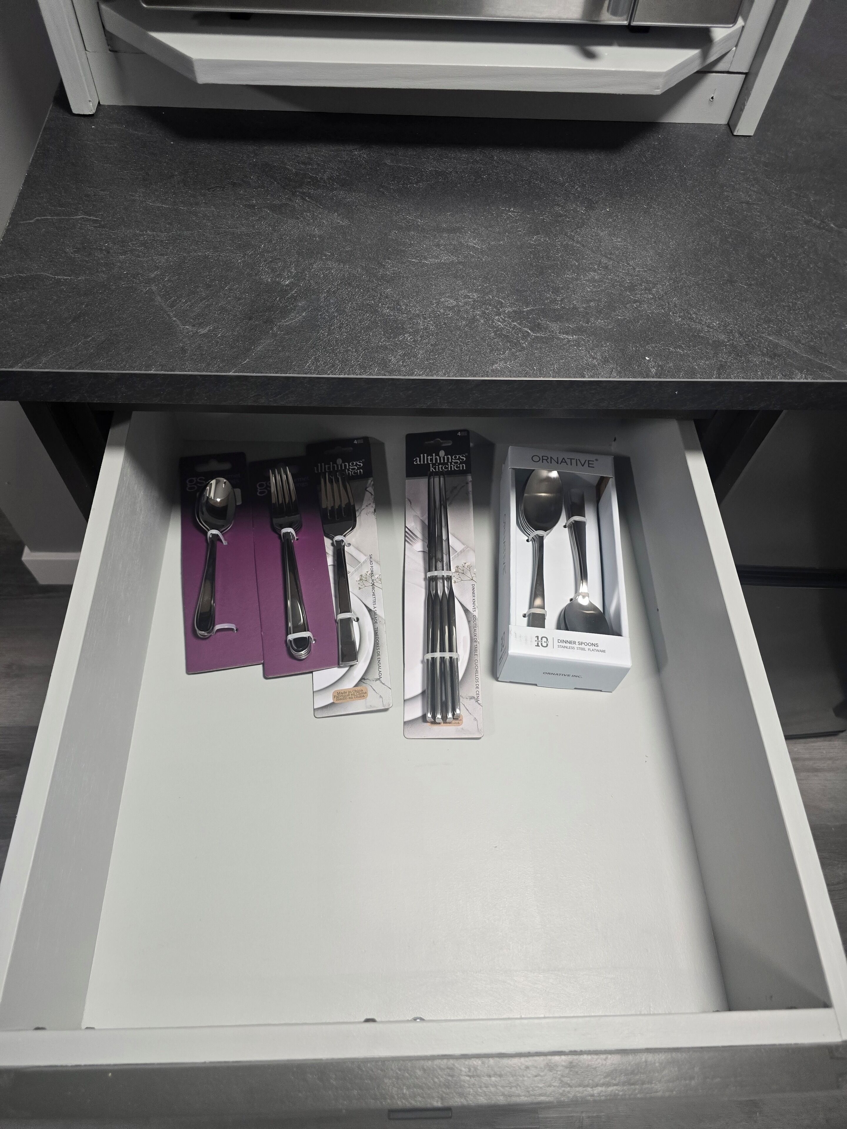 Un cajón con varios utensilios de cocina, incluyendo cucharas, tenedores y un juego de 10 cucharadas para servir.