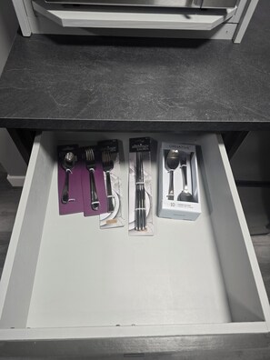 Eine Schublade mit verschiedenen Küchenutensilien, darunter Löffel, Gabeln und ein Set mit zehn Esslöffeln.