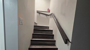 Una escalera con peldaños oscuros y una barandilla metálica, que conduce a un rellano con un extintor.