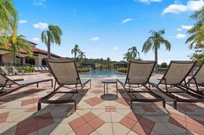 A poolside area with lounge chairs, a tiled floor, and palm trees. - Sweet Retreat At Bella Vida (Kissimmee)