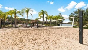 Una cancha de voleibol de playa con arena, una red, rodeada de palmeras y un cielo despejado.