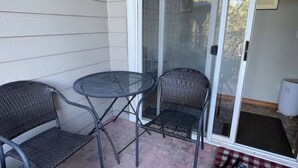 En liten uteplats med två fåtöljer i rotting och ett bord i glas, intill en skjutdörr av glas.