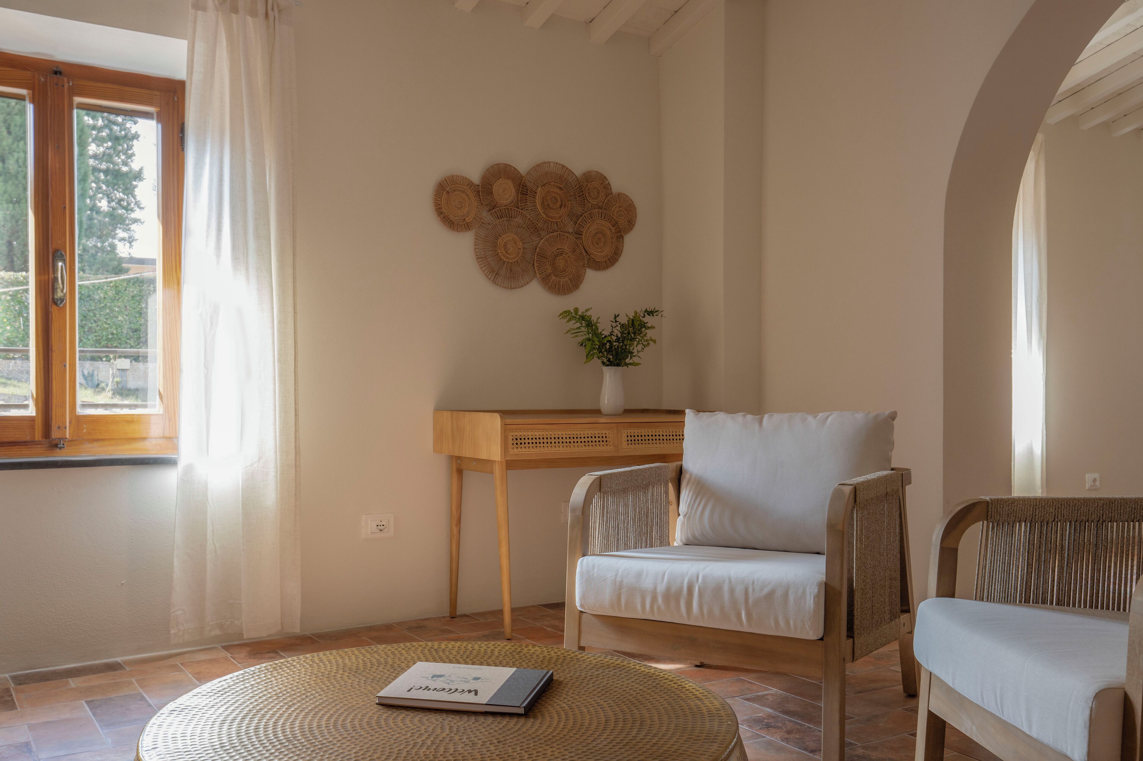 A cozy room with a round woven rug, a wooden side table with a plant, a white sofa, and a wicker chair.