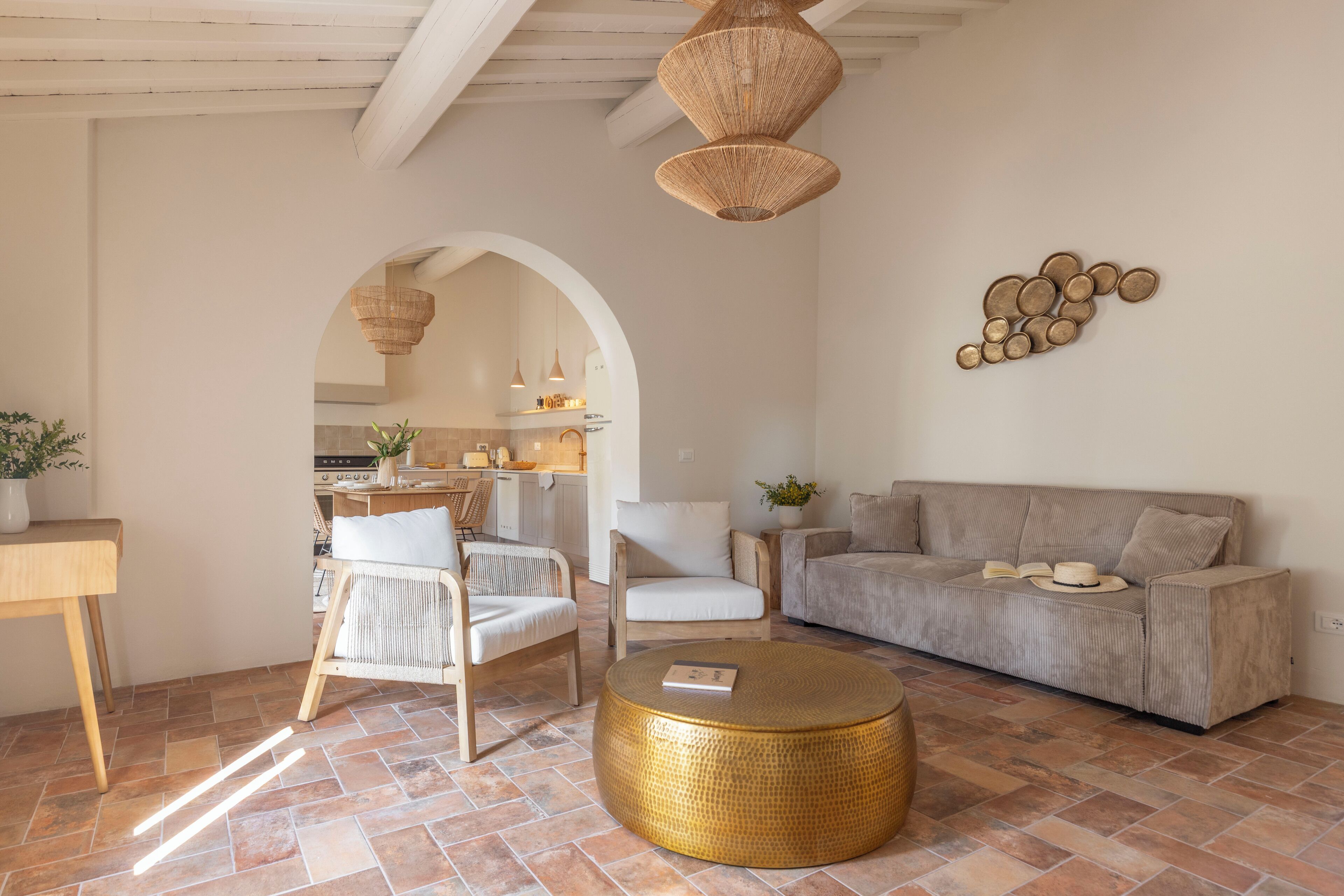 Ein Wohnzimmer mit einer Couch, Sesseln, einem Couchtisch und einer Küche im Hintergrund.