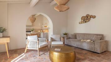 Ein Wohnzimmer mit einer Couch, Sesseln, einem Couchtisch und einer Küche im Hintergrund.