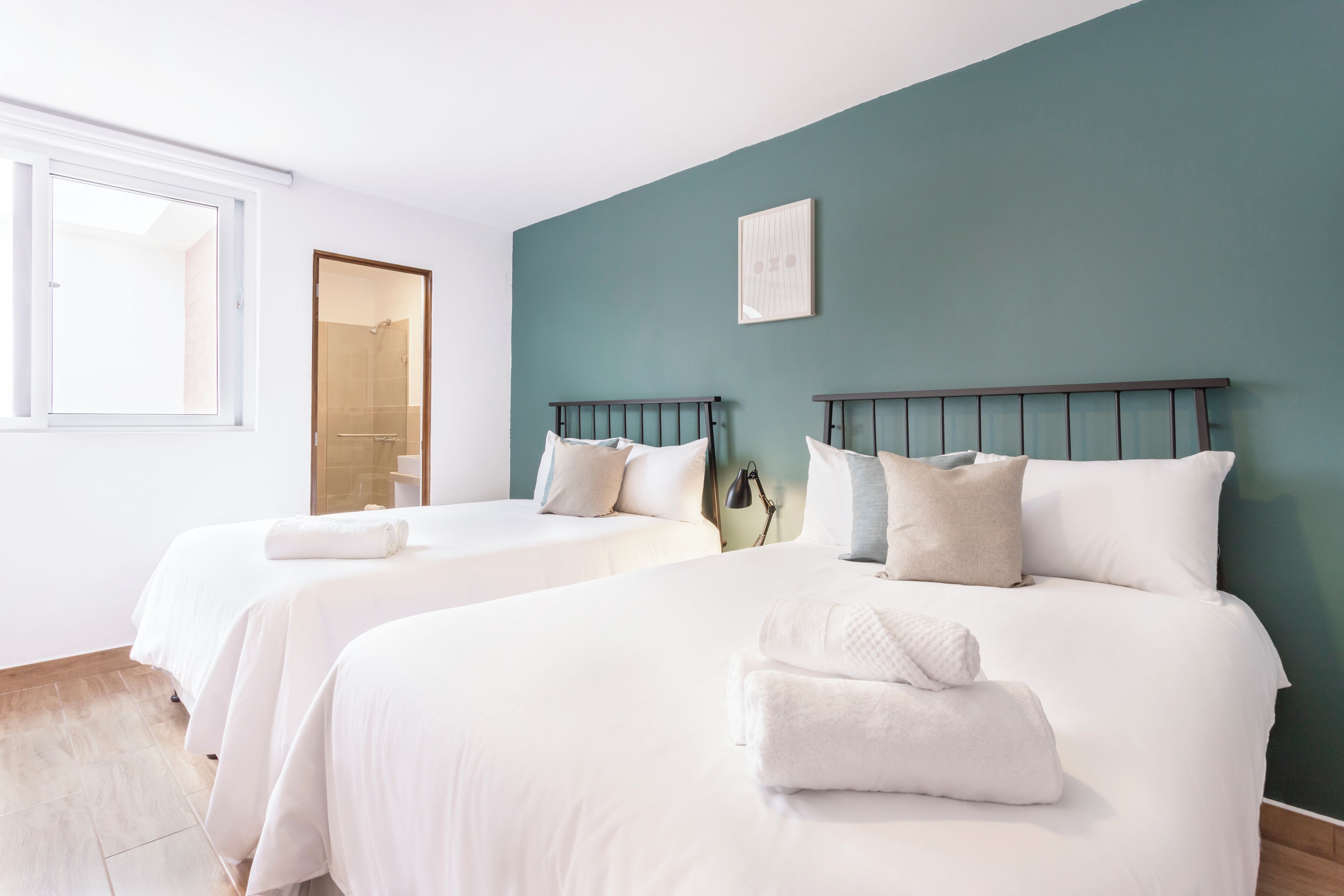 A hotel room with two beds, a window, and a teal-colored wall.