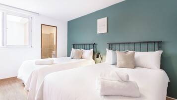 A hotel room with two beds, a window, and a teal-colored wall.