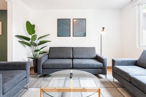 Uma sala de estar moderna com um sofá cinzento, uma mesa de centro e uma planta em vaso.