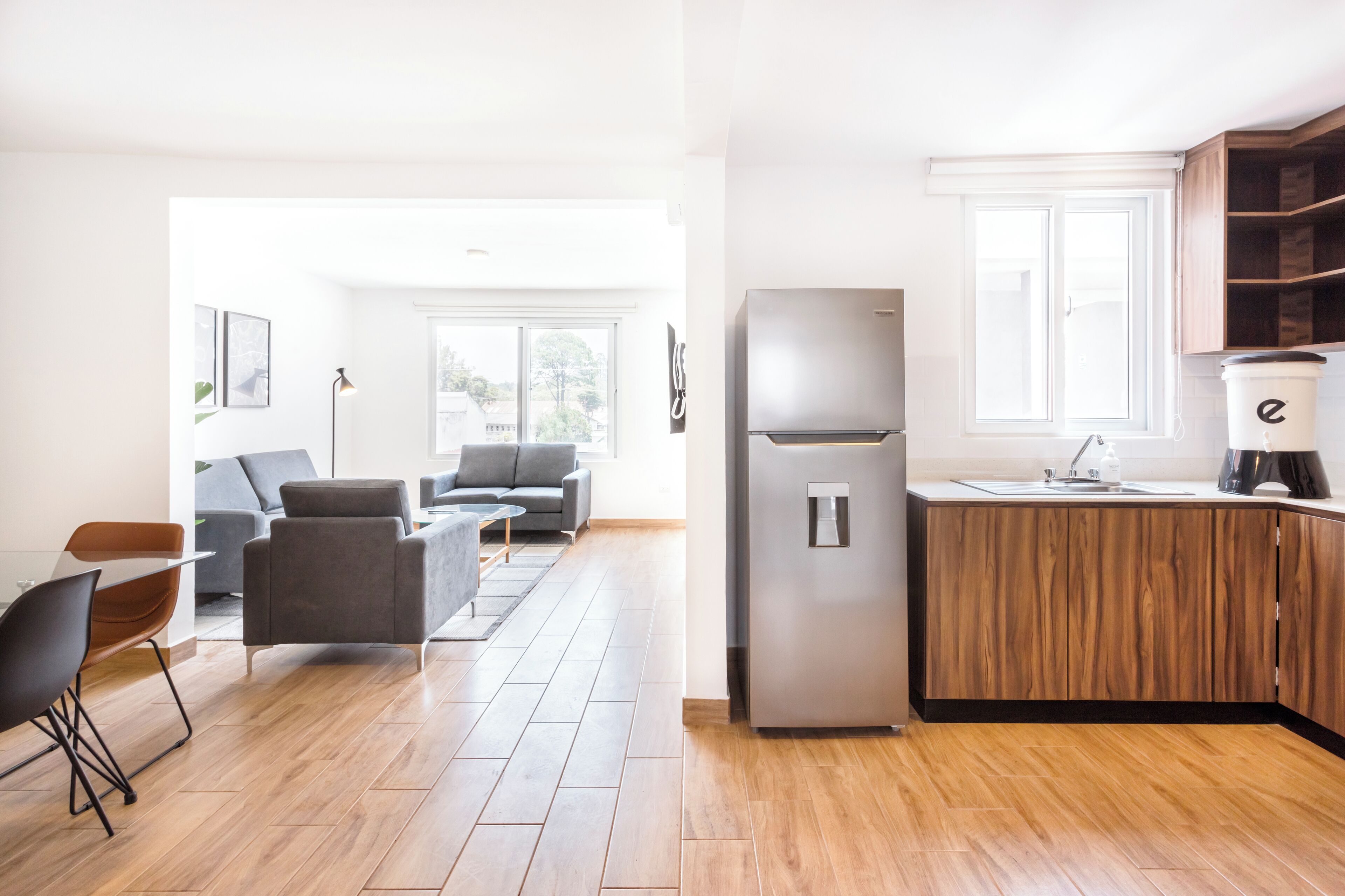 Una cocina moderna con refrigerador empotrado y muebles de madera, un comedor con mesa y sillas, y una sala de estar con sofá y una mesita de centro.