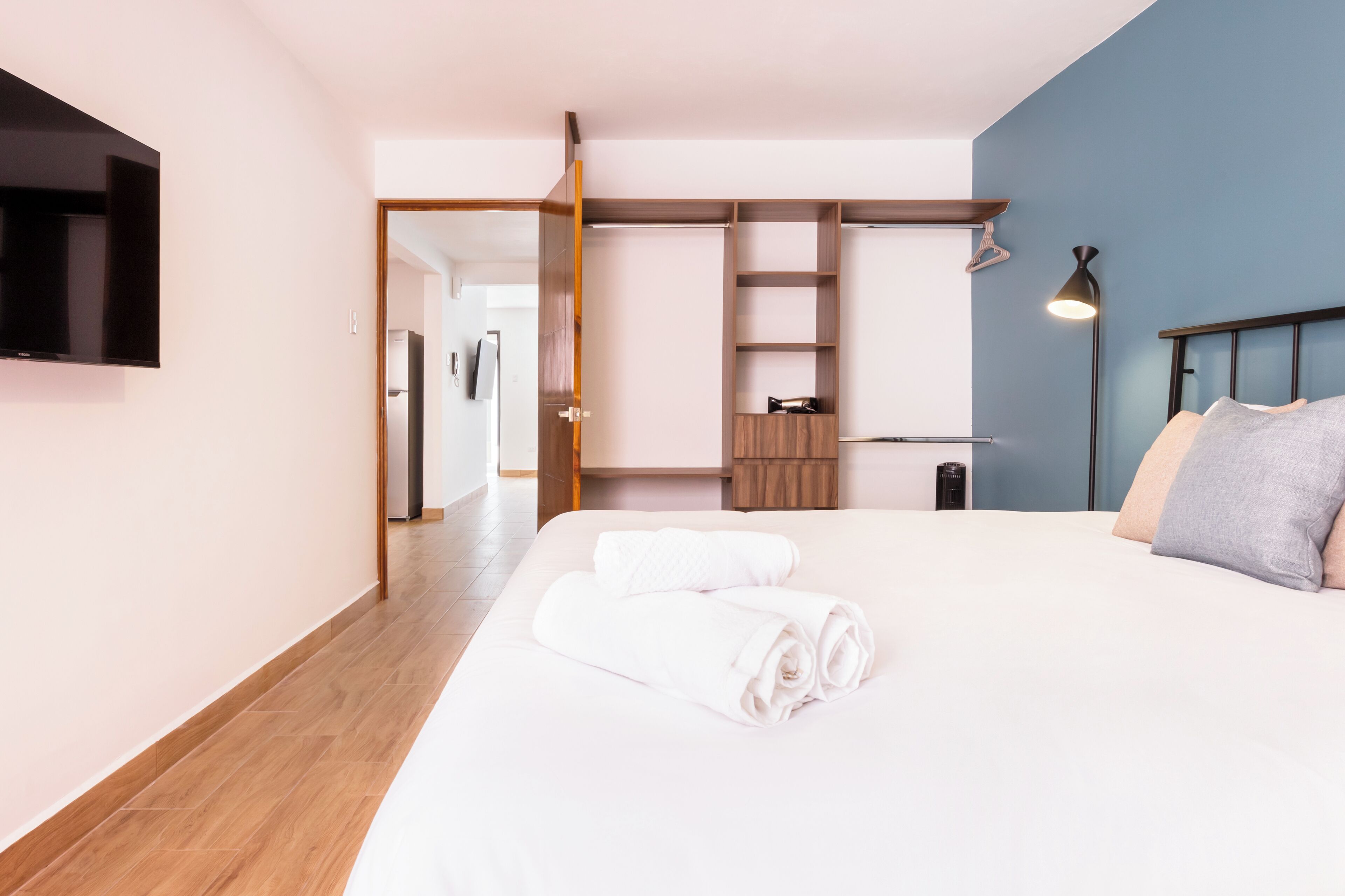 Une chambre d’hôtel moderne dotée d’un grand lit, d’un téléviseur à écran plat fixé au mur, d’une armoire et d’un bureau avec une lampe.