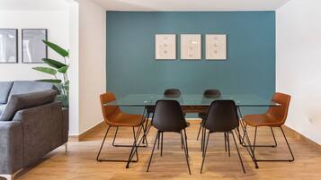 Un comedor moderno con una mesa de vidrio y sillas negras y marrones, un sofá gris y una pared de acento color verde azulado.
