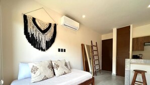 Une chambre avec un lit, une décoration murale en macramé, un climatiseur, une échelle et un coin cuisine.