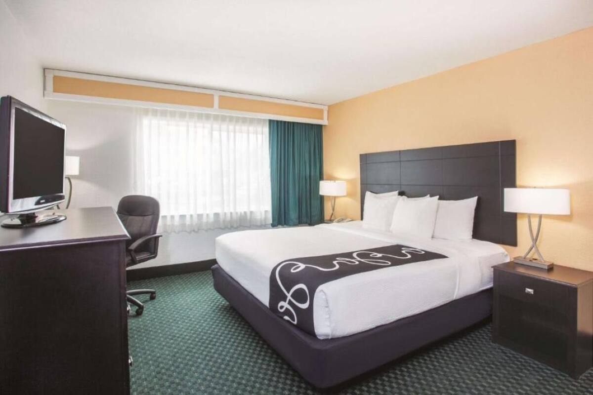 A hotel room with a bed, a desk, a chair, a TV, and a window with curtains.