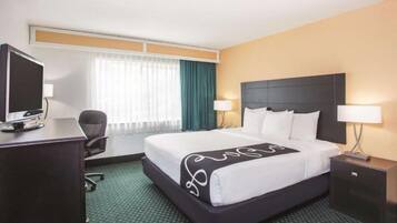 Ein Hotelzimmer mit Bett, Schreibtisch, Stuhl, Fernseher und einem Fenster mit Vorhängen.