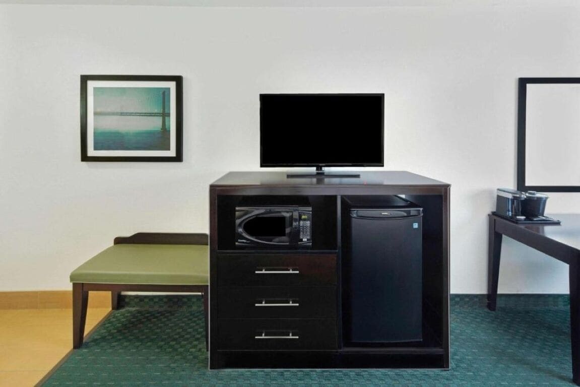 A compact room with a desk, a television, a microwave, and a small refrigerator.