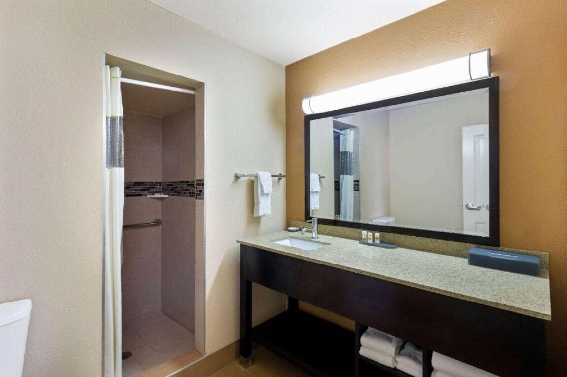 Un baño con ducha, lavamanos y espejo.