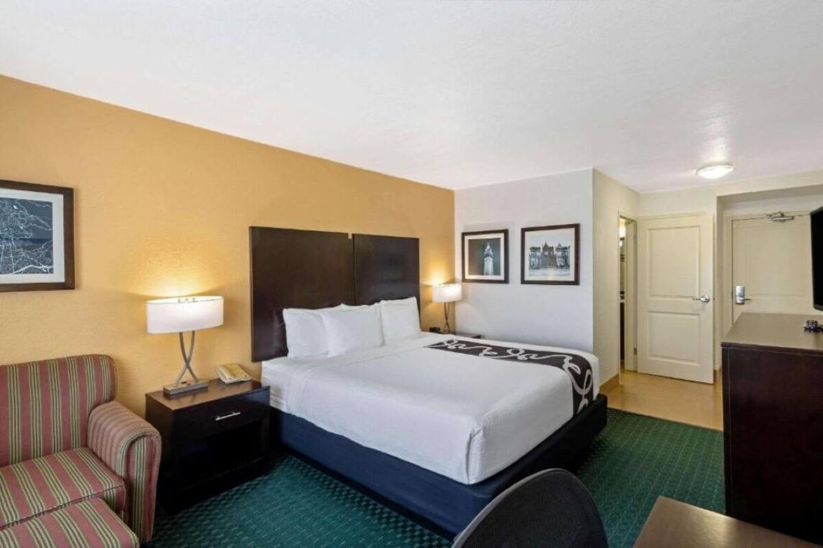 A hotel room with a bed, a chair, a desk, and a wardrobe.