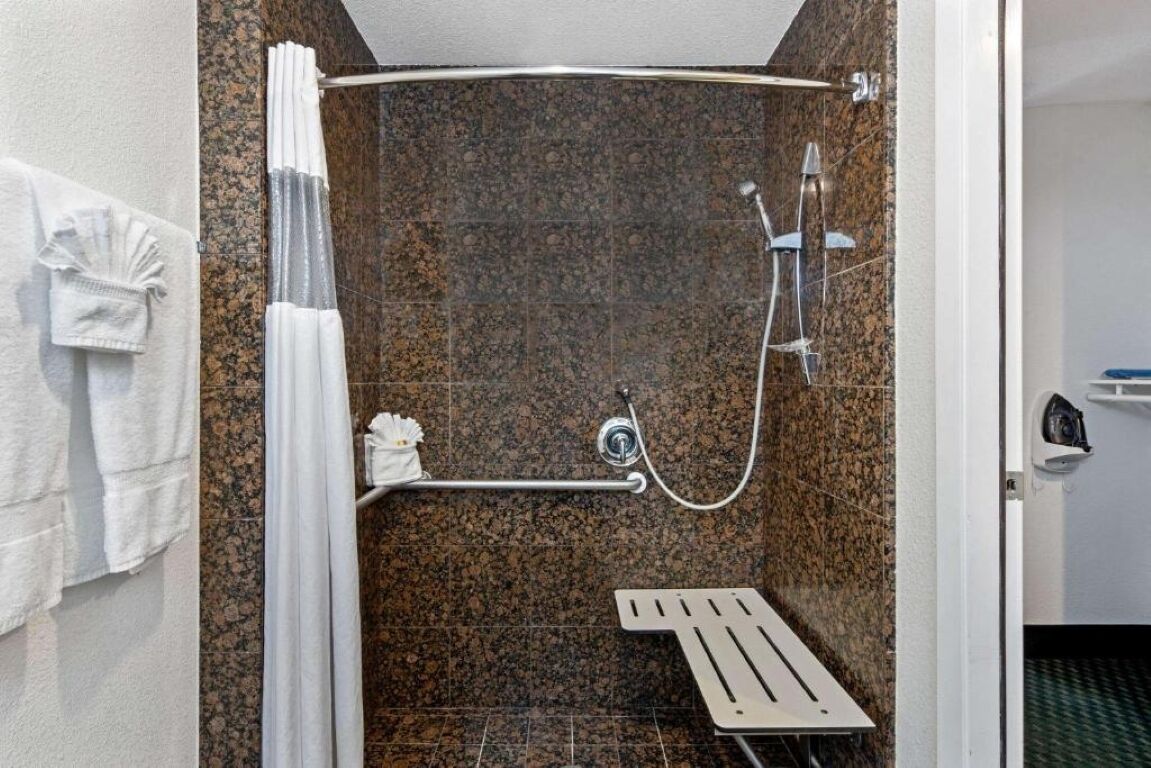 Un área de ducha con ducha de techo curva, ducha de mano y barra de apoyo.