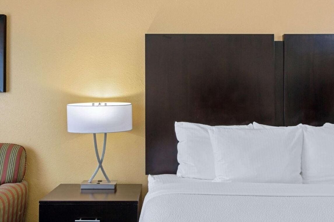 A hotel room with a bed, a nightstand with a lamp, and a striped chair.
