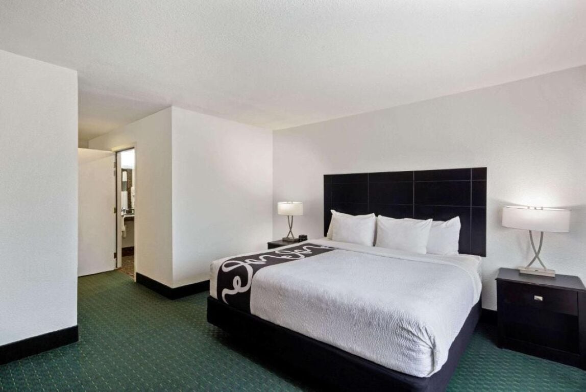 A hotel room with a large bed, two bedside tables, a headboard, and a carpeted floor.