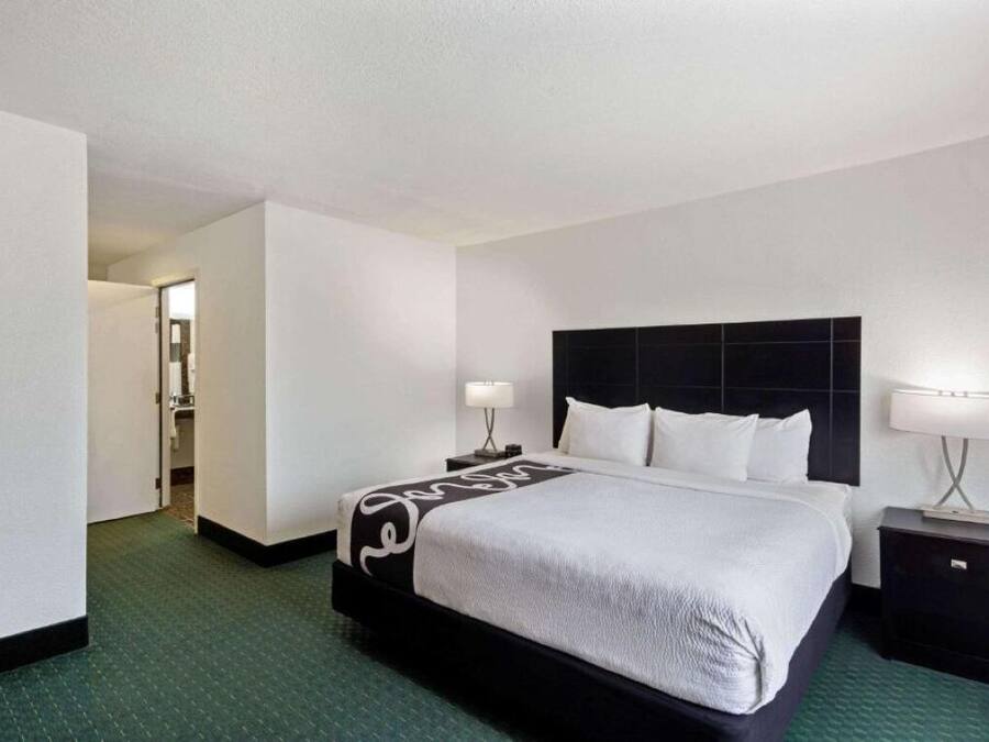 A hotel room with a large bed, two bedside tables, a headboard, and a carpeted floor.
