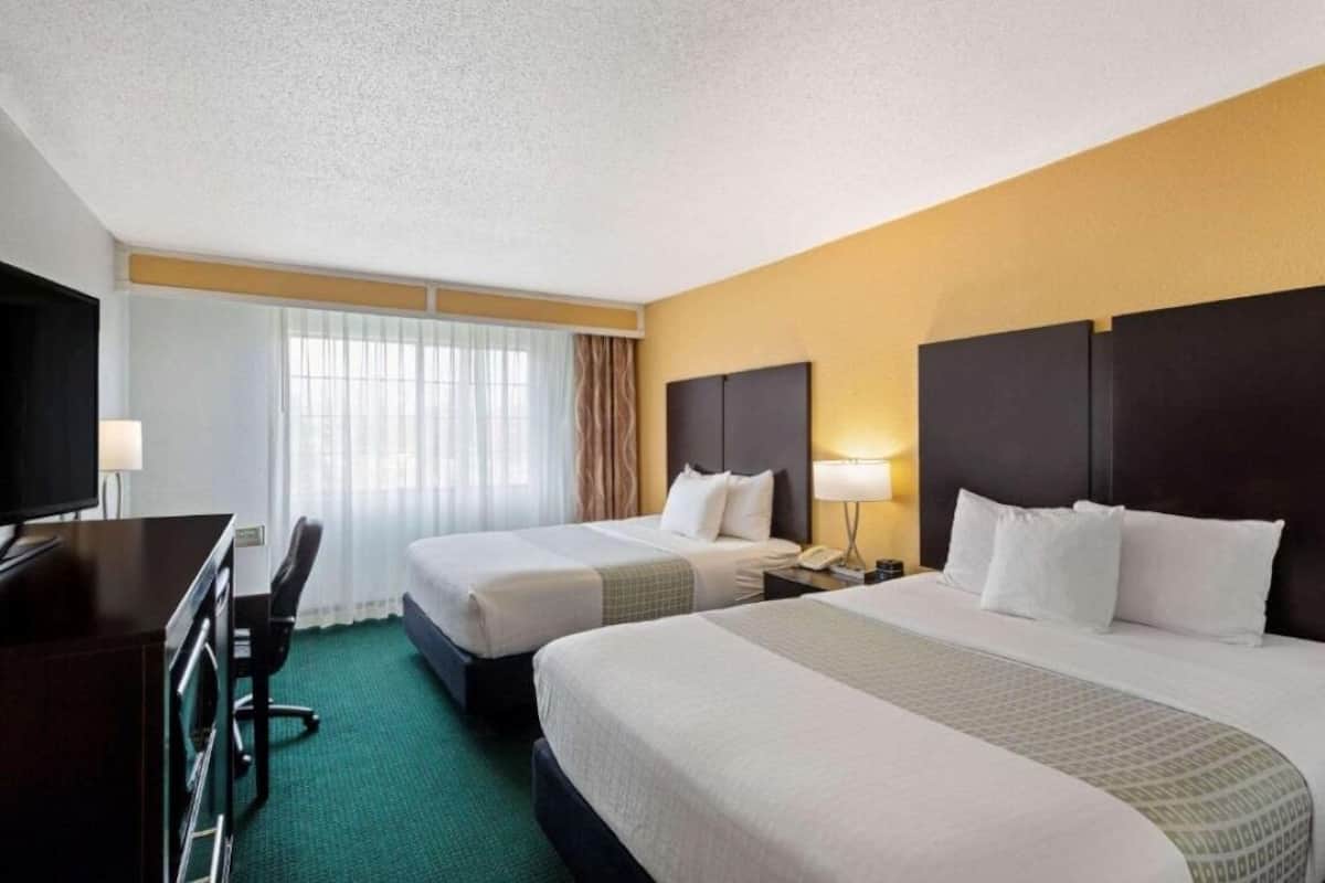 A hotel room with two beds, a desk, and a TV.