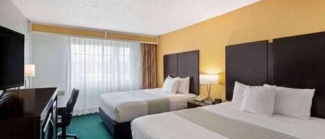 A hotel room with two beds, a desk, and a TV.