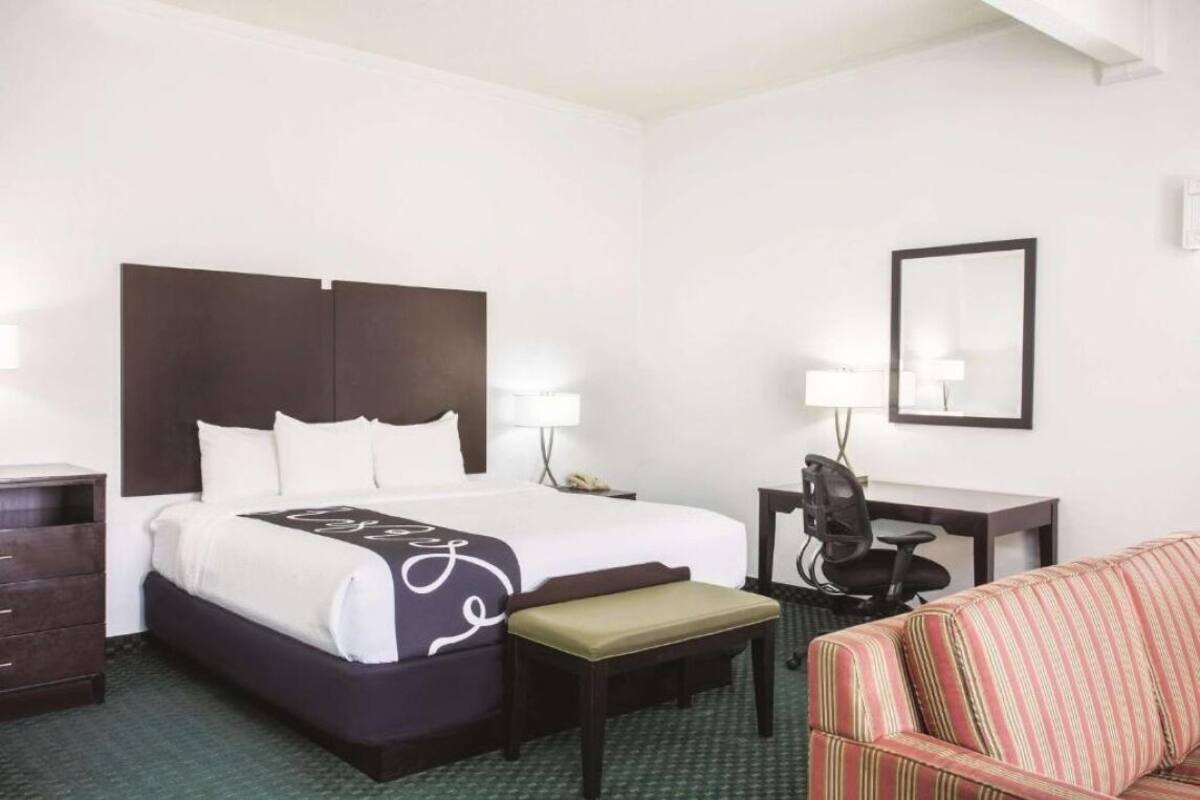 A hotel room with a large bed, a desk with a chair, a small table, a bench, and a sofa.