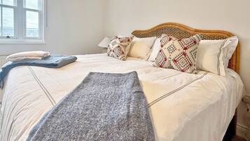 A neatly made bed with a patterned headboard, a window with blinds, and a bedside table with a lamp.