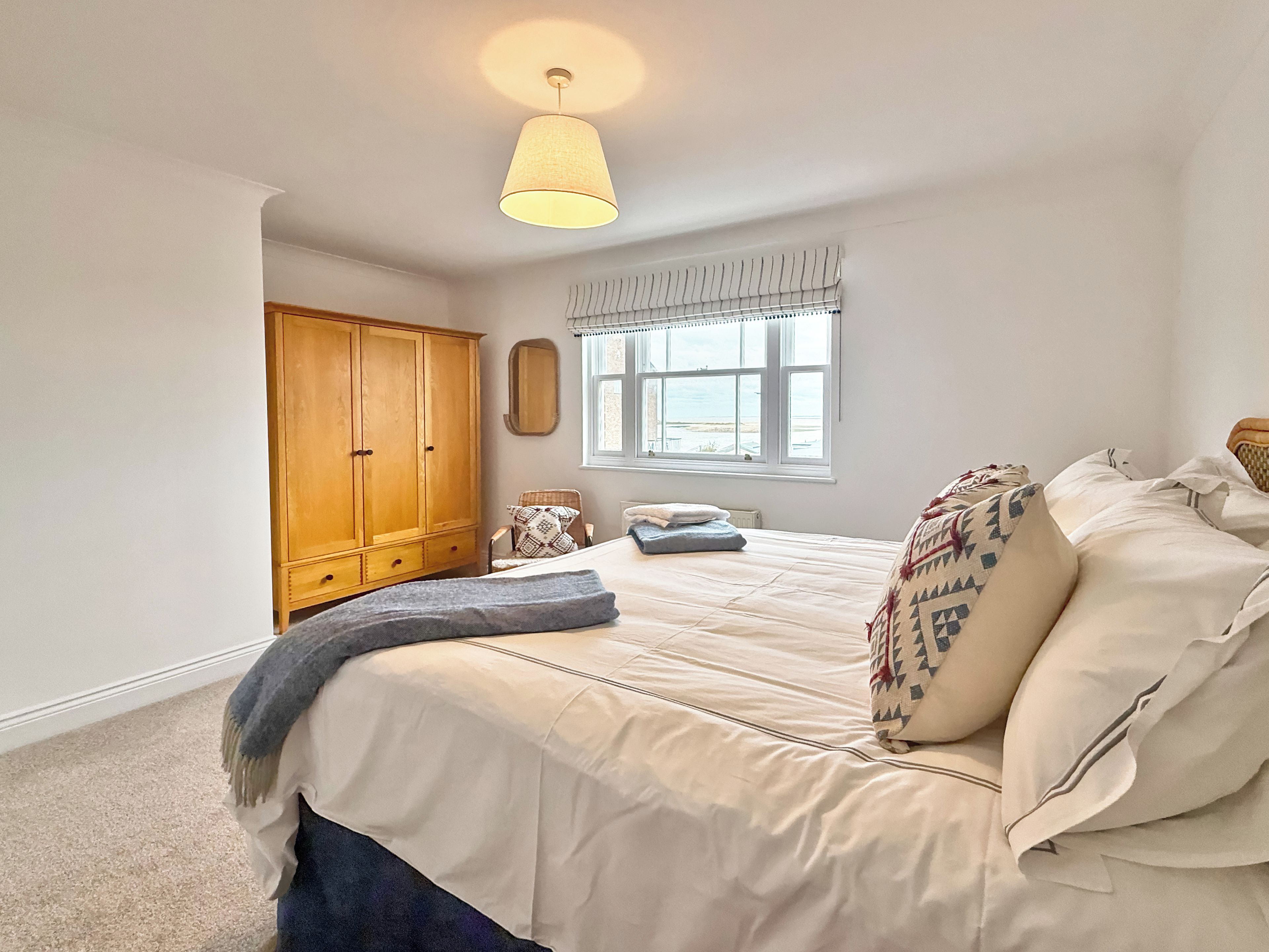 A bedroom with a bed, a wardrobe, a window, and a hanging light fixture.