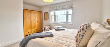 A bedroom with a bed, a wardrobe, a window, and a hanging light fixture.