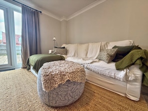Ein Wohnzimmer mit einer Couch, einem Hocker und Blick ins Freie durch ein großes Fenster.