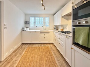 A kitchen with white cabinets, a wooden floor, a window, and a green towel hanging on the oven.
