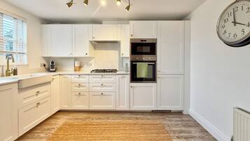 A kitchen with white cabinets, a clock, and a woven rug.