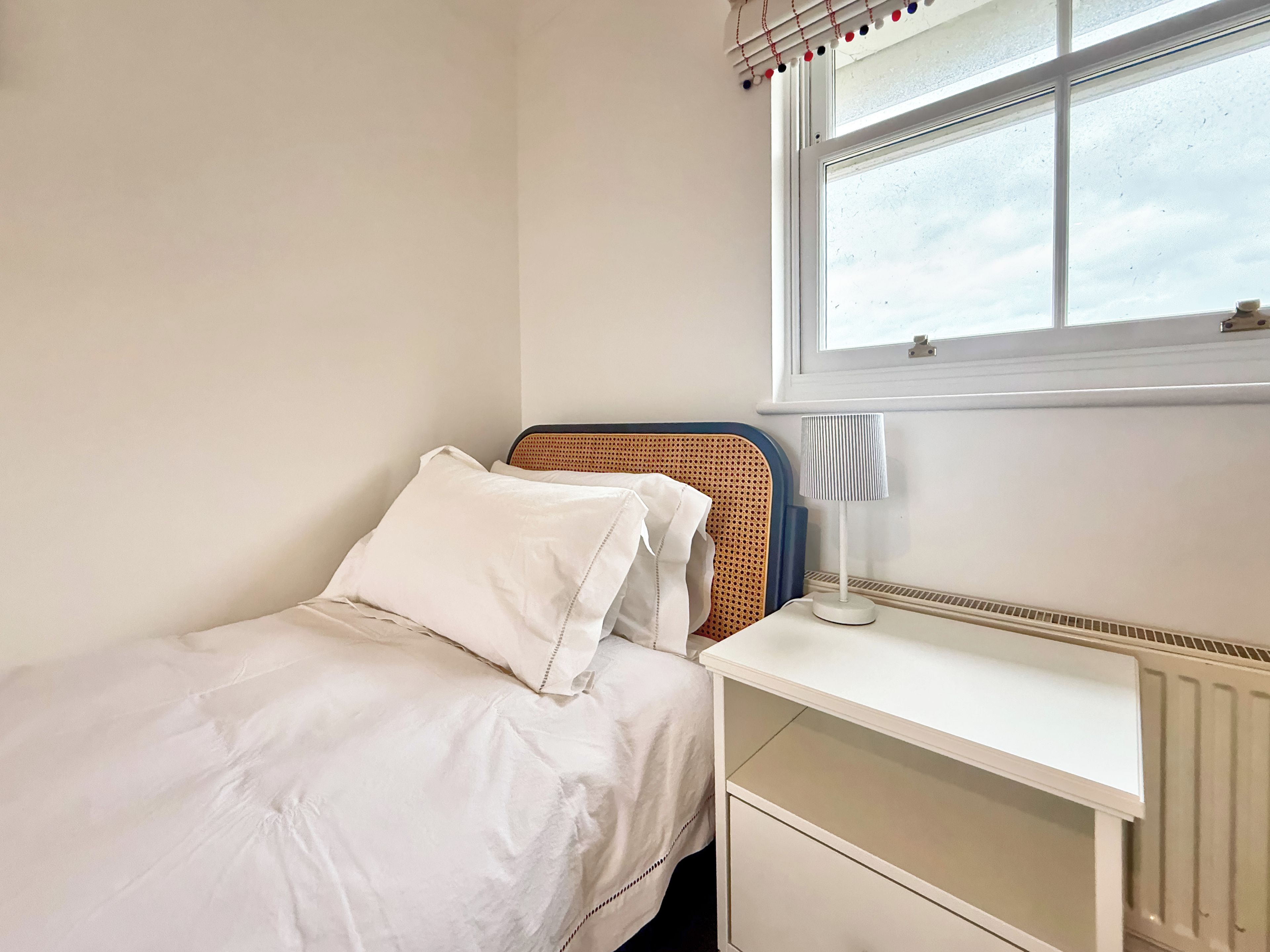 Un dormitorio con cama, mesita de noche, lámpara y ventana.