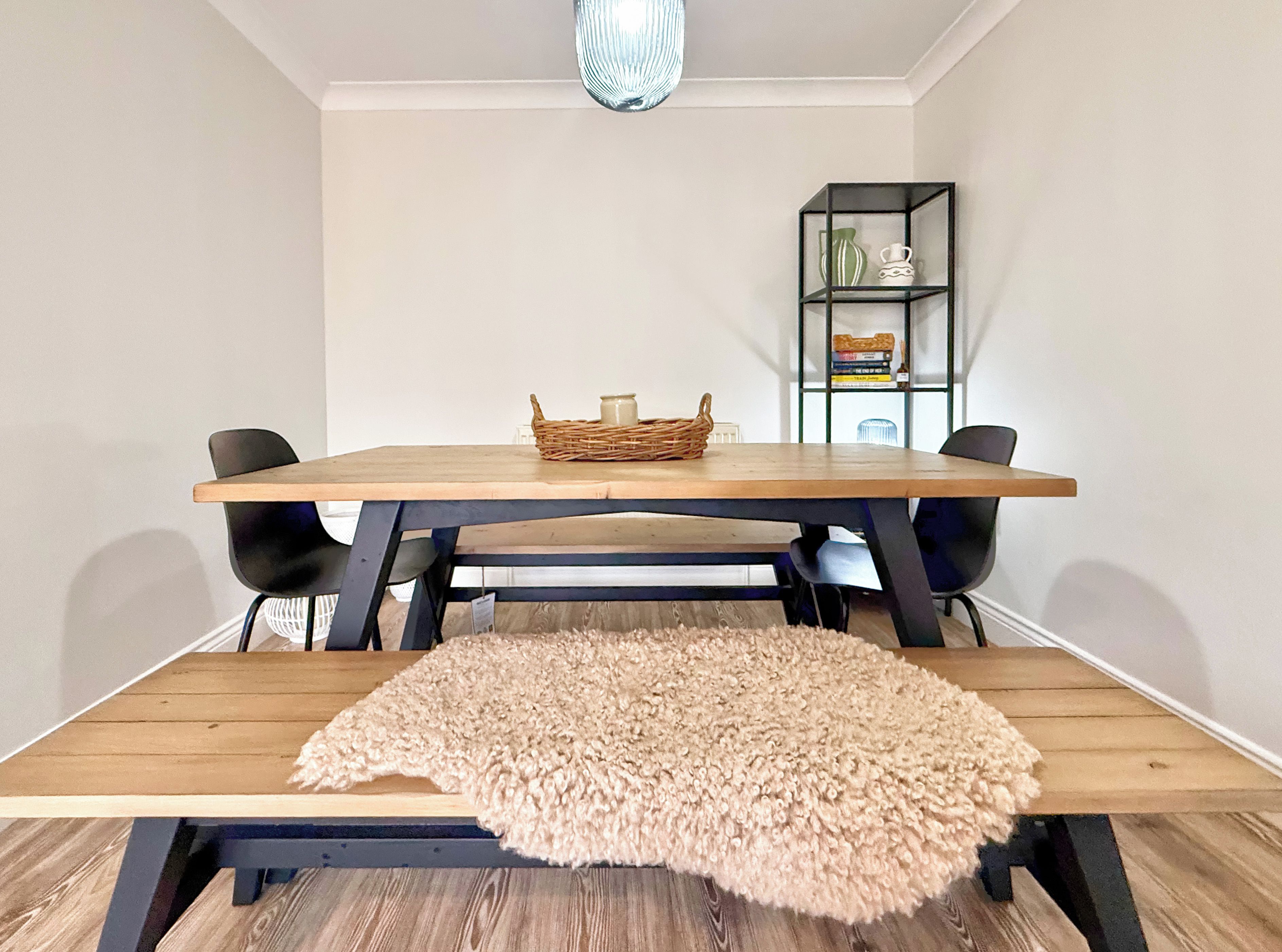 A dining area with a wooden table, black chairs, a woven basket, and a fluffy rug.