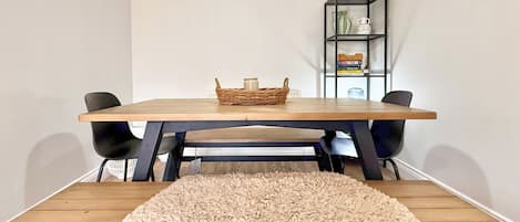 Een eetgedeelte met een houten tafel, zwarte stoelen, een rieten mand en een zacht tapijt.