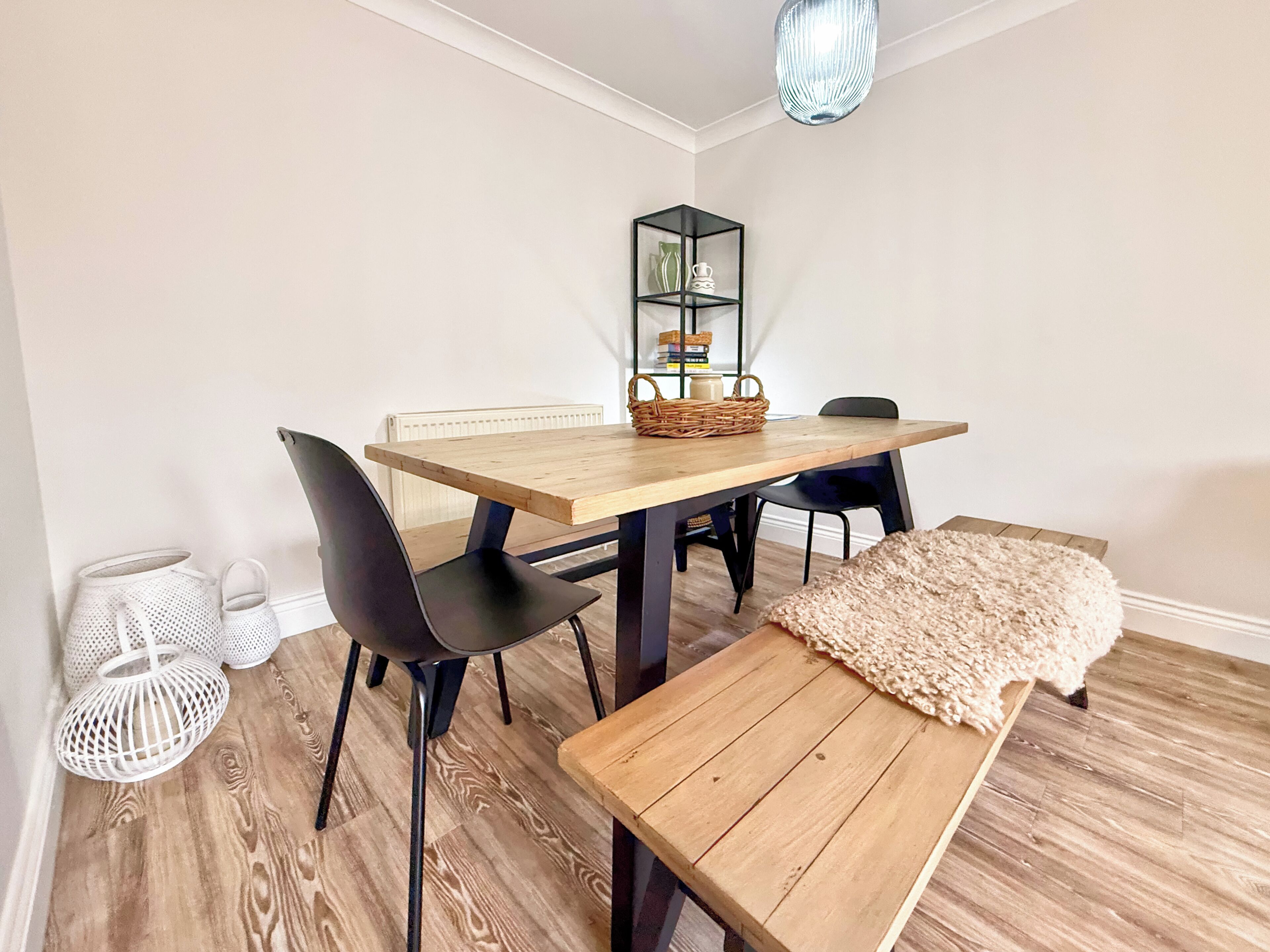 Een eethoek met een houten tafel, zwarte stoelen, een bank, een geweven mand en een hangende lamp.