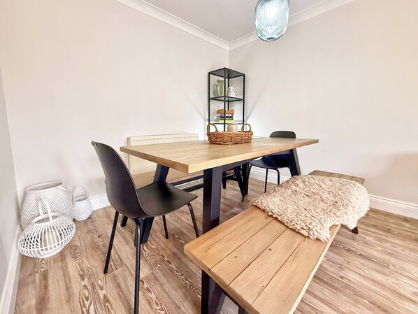 A dining area with a wooden table, black chairs, a bench, a woven basket, and a hanging light fixture.