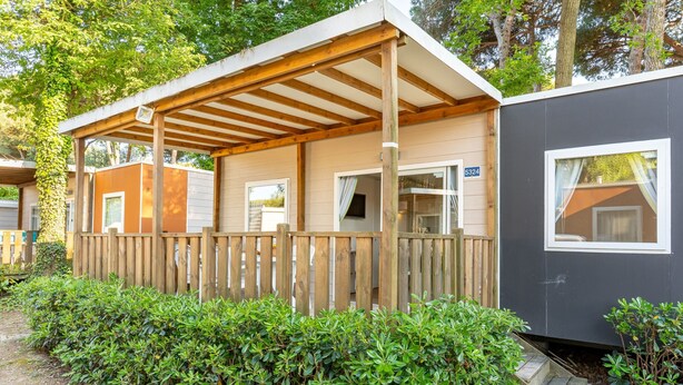 Un pontile in legno con una zona coperta, un piccolo edificio con una finestra e un siepe di fronte.