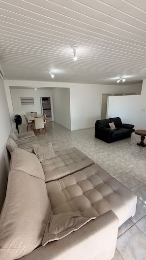 A spacious living area with a sectional sofa, a black sofa, a dining table with chairs, and a kitchen in the background. - Dom João Becker (Florianópolis)
