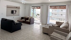 Un soggiorno spazioso con un'ampia televisione, posti a sedere confortevoli e vista sull'esterno.