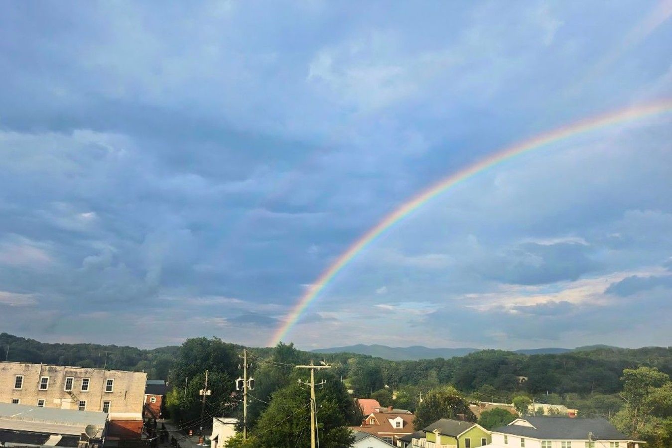 A rainbow arching over a residential area with houses and utility poles.