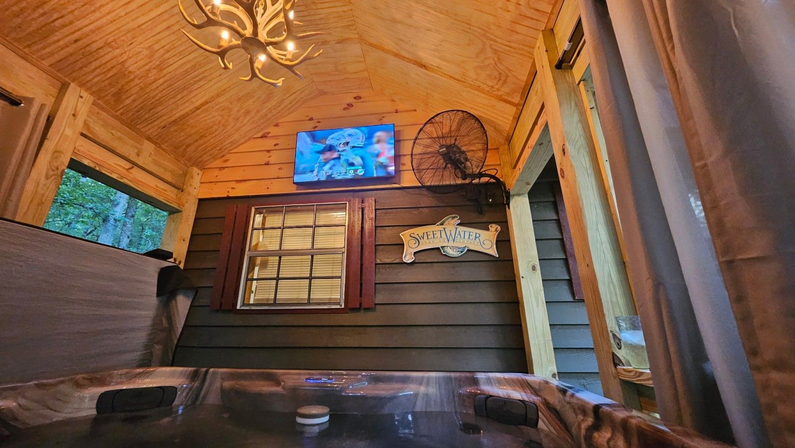 Ein Holzblockhaus-Interieur mit Whirlpool, einem an der Wand montierten Fernseher und einem Schild mit der Aufschrift 'SweetWater'.