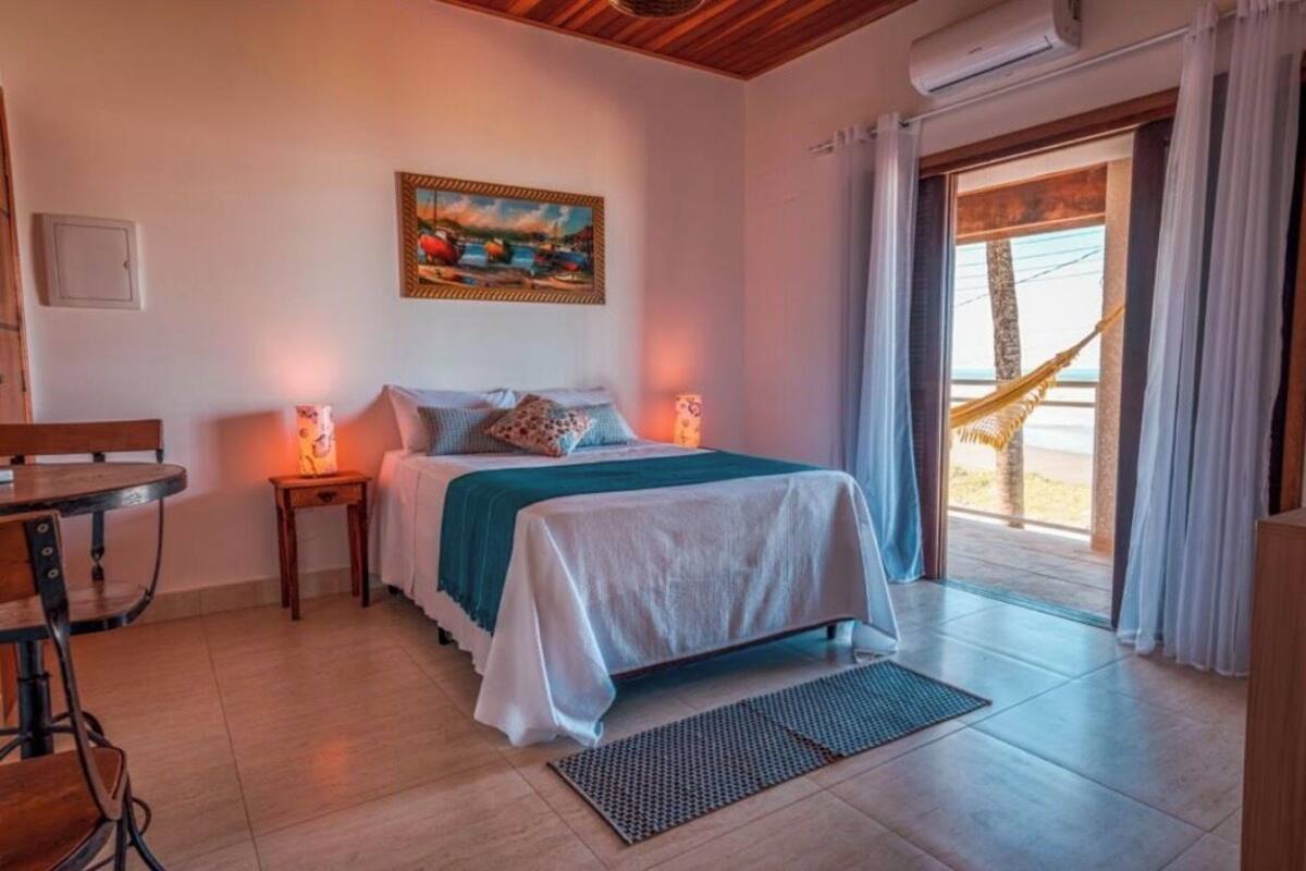 Une chambre avec un lit, une table de chevet, une table et un hamac près de la fenêtre.