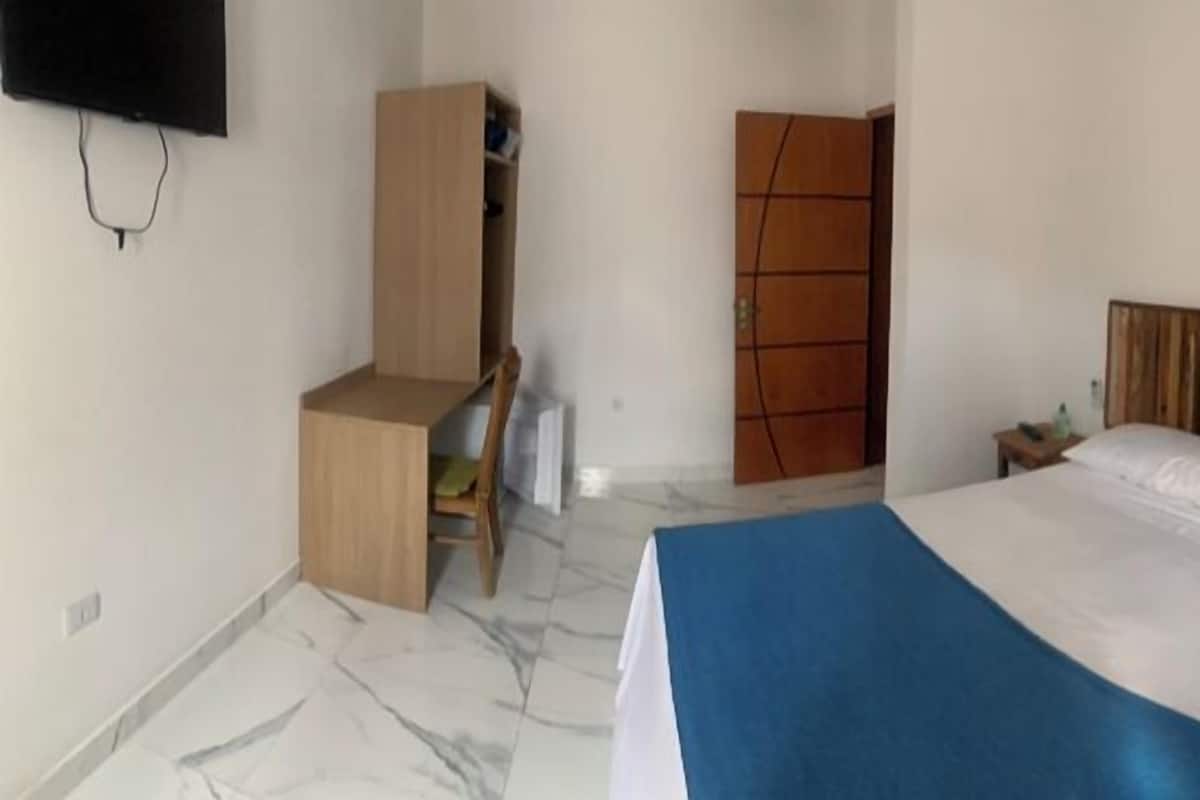 Une chambre d’hôtel avec un lit, une armoire en bois, un téléviseur fixé au mur et une petite table de chevet.