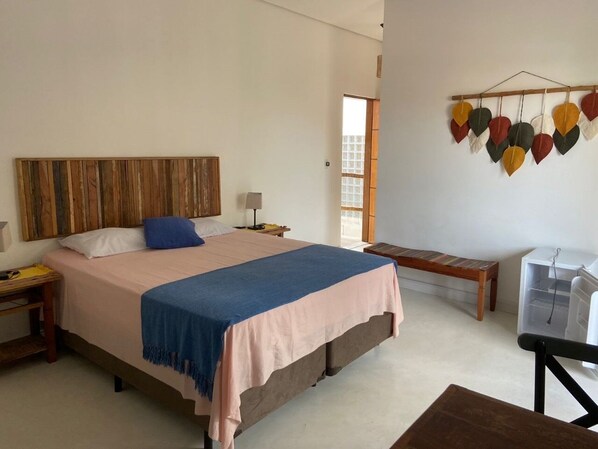 Een slaapkamer met een groot bed, een houten hoofdbord, een bankje, een klein tafeltje en een decoratie aan de muur.
