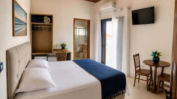 Quarto de hotel com cama, escrivaninha, cadeira, televisão e banheiro.