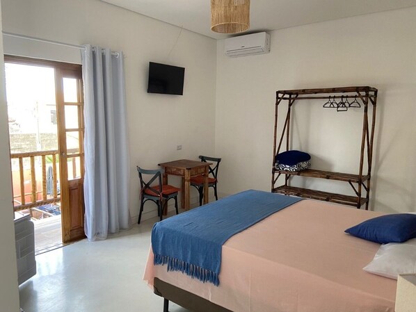 A bedroom with a bed, a TV, a table with chairs, and a wooden chair. - Nudist Inn in Peruíbe (Peruíbe)